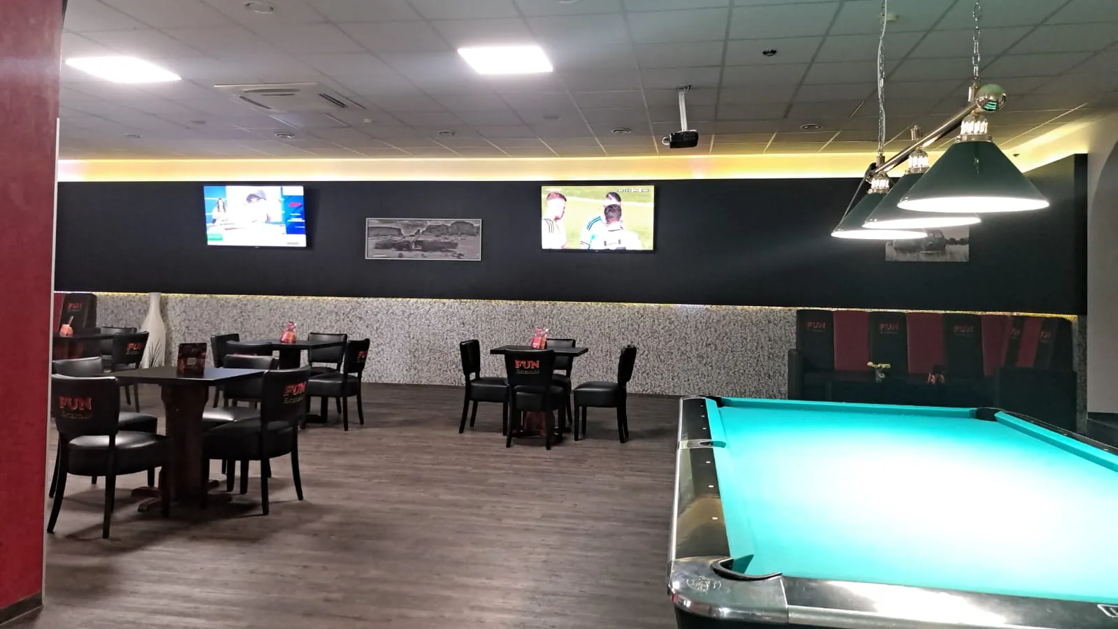 Pooltisch mit türkisfarbenem Tuch unter schwarzen Lampen in der Players Lounge Wesel, dahinter Tische, Stühle und Fernseher an der Wand