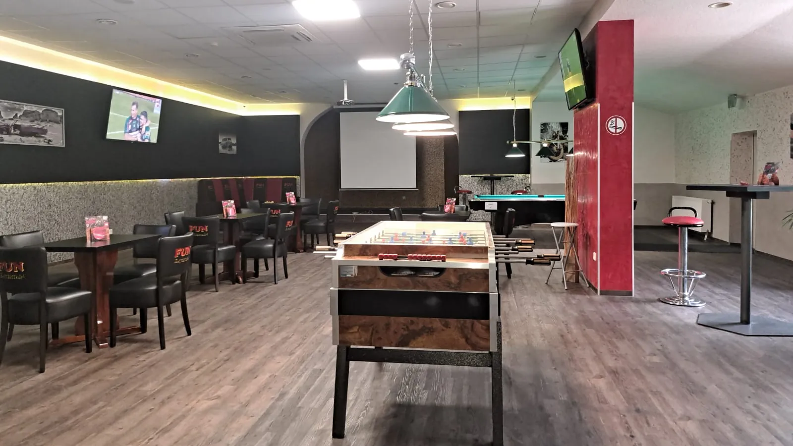 Kicker im Holzdekor mitten im Gastraum der Sportsbar Wesel, dahinter Tische mit Ledersesseln, Fernseher an den Wänden und eine Leinwand