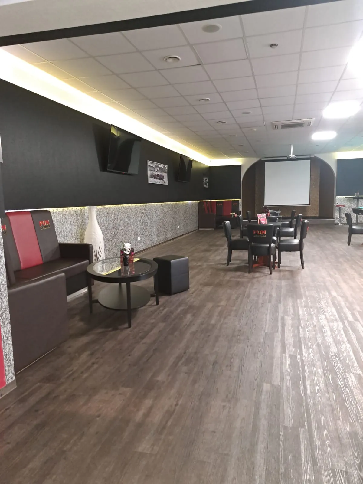 Sofaecke der Sportsbar Wesel mit dunklem Ledersofa, roten Rückenkissen, rundem Glastisch und großer weißer Vase